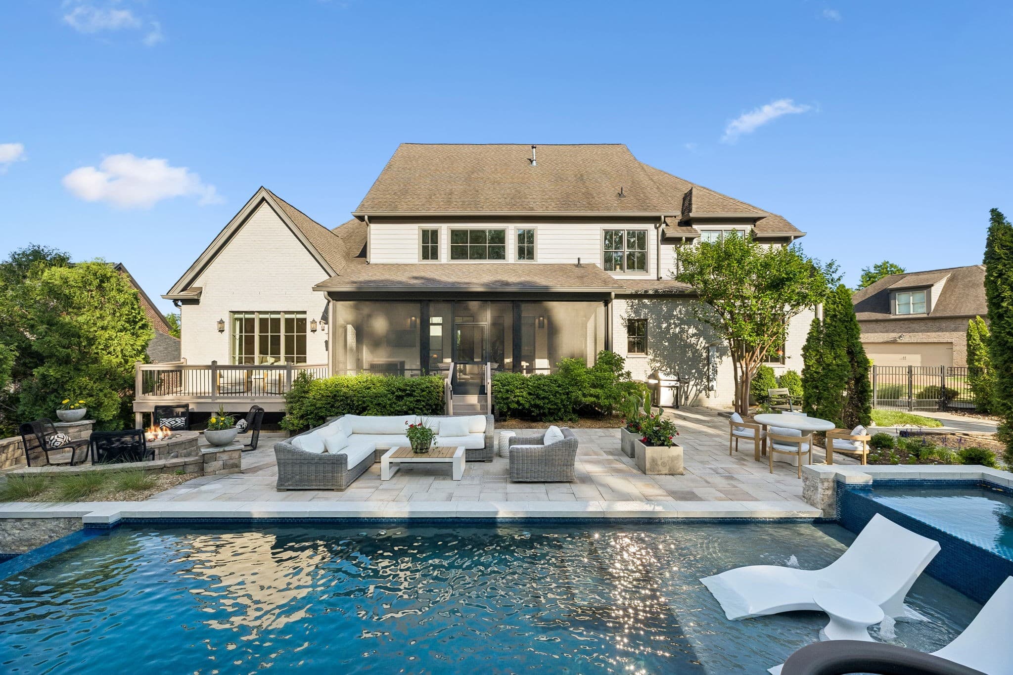 Rear exterior of a painted brick Brentwood, Tennessee estate with a screened porch, stone patio, and pool with spa