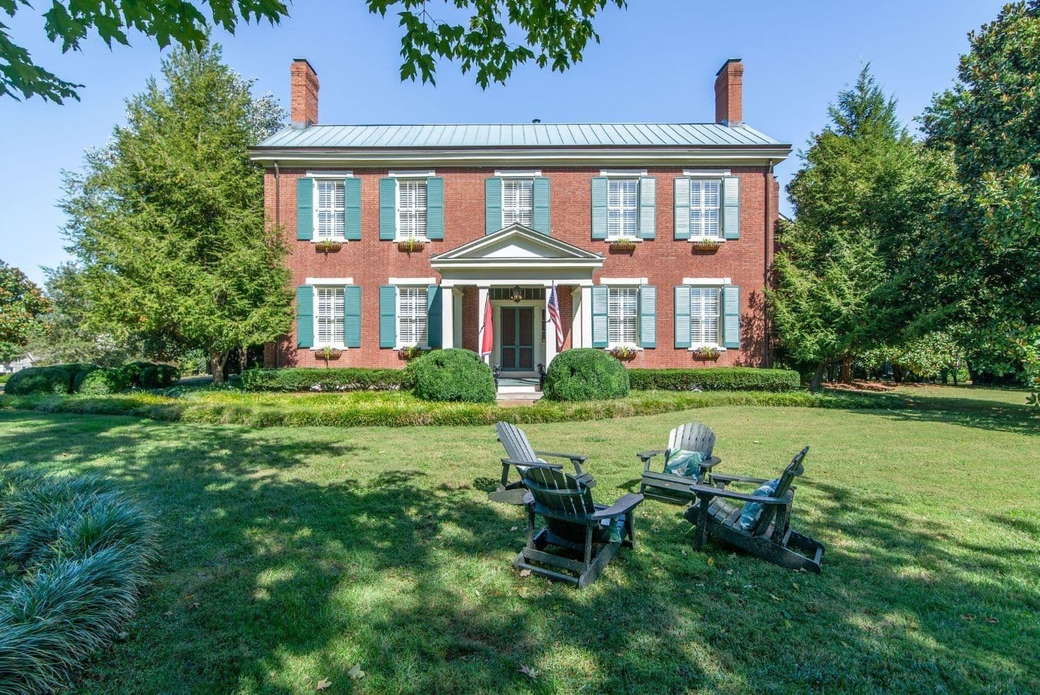 Historic Federal-style brick estate with painted shutters behind boxwood hedges and mature trees