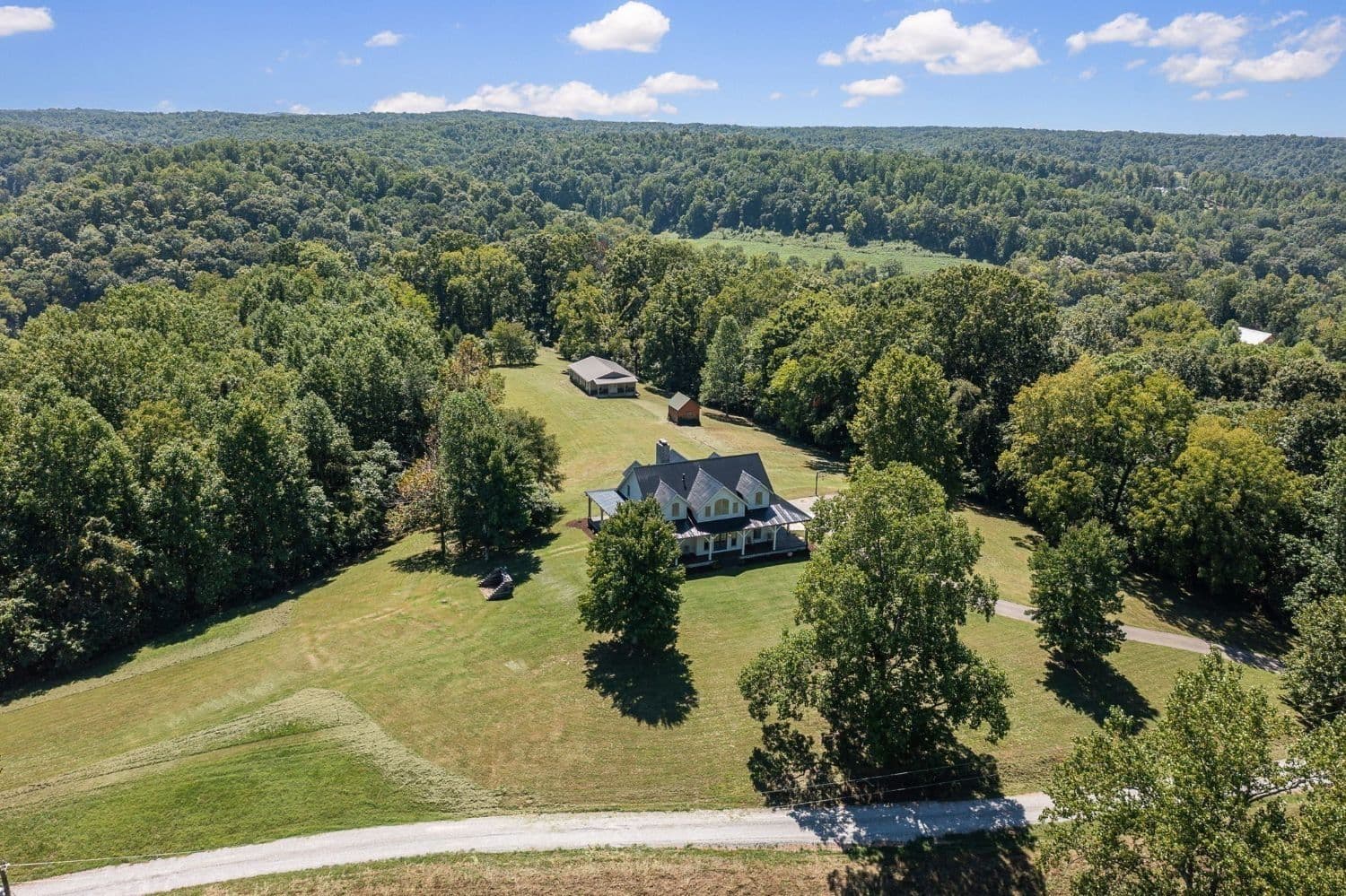 Aerial view of a farmhouse and barn on wooded acreage near Leipers Fork