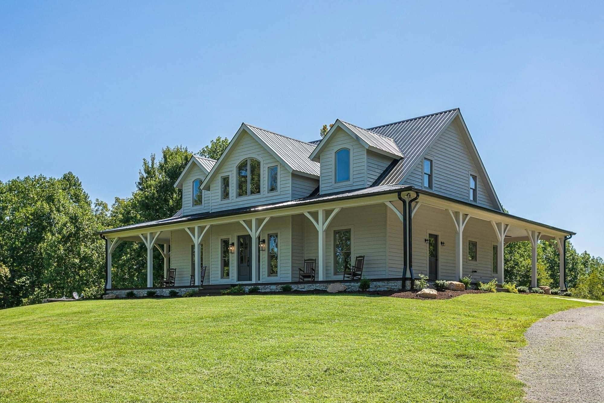 White farmhouse with wraparound porch and metal roof on a hilltop lawn in Williamson County
